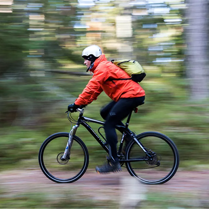 En cyklist med röd jacka i skogen.