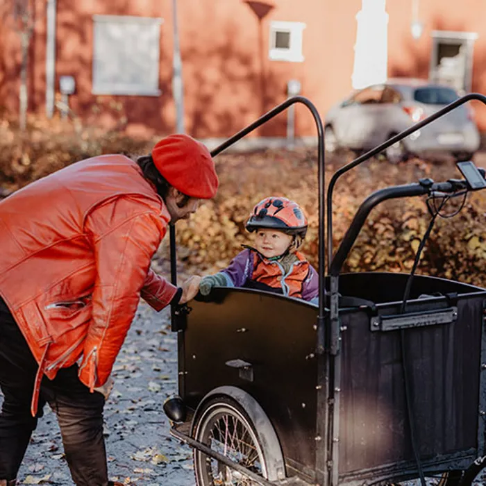 En pappa står vid sitt barn som sitter i en cykelvagn.