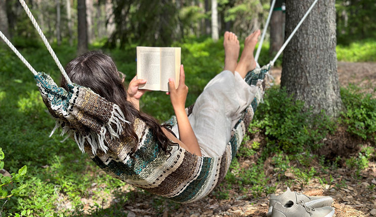 A person is lying in a hammock in the forest by Tomtebo Strand, reading a book