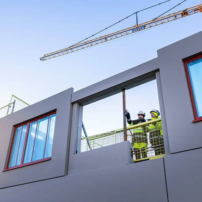 wo construction workers are standing and looking out from a house construction site