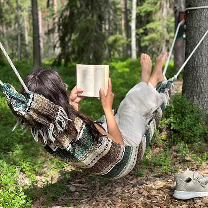 A person is reading a book in a hammock.